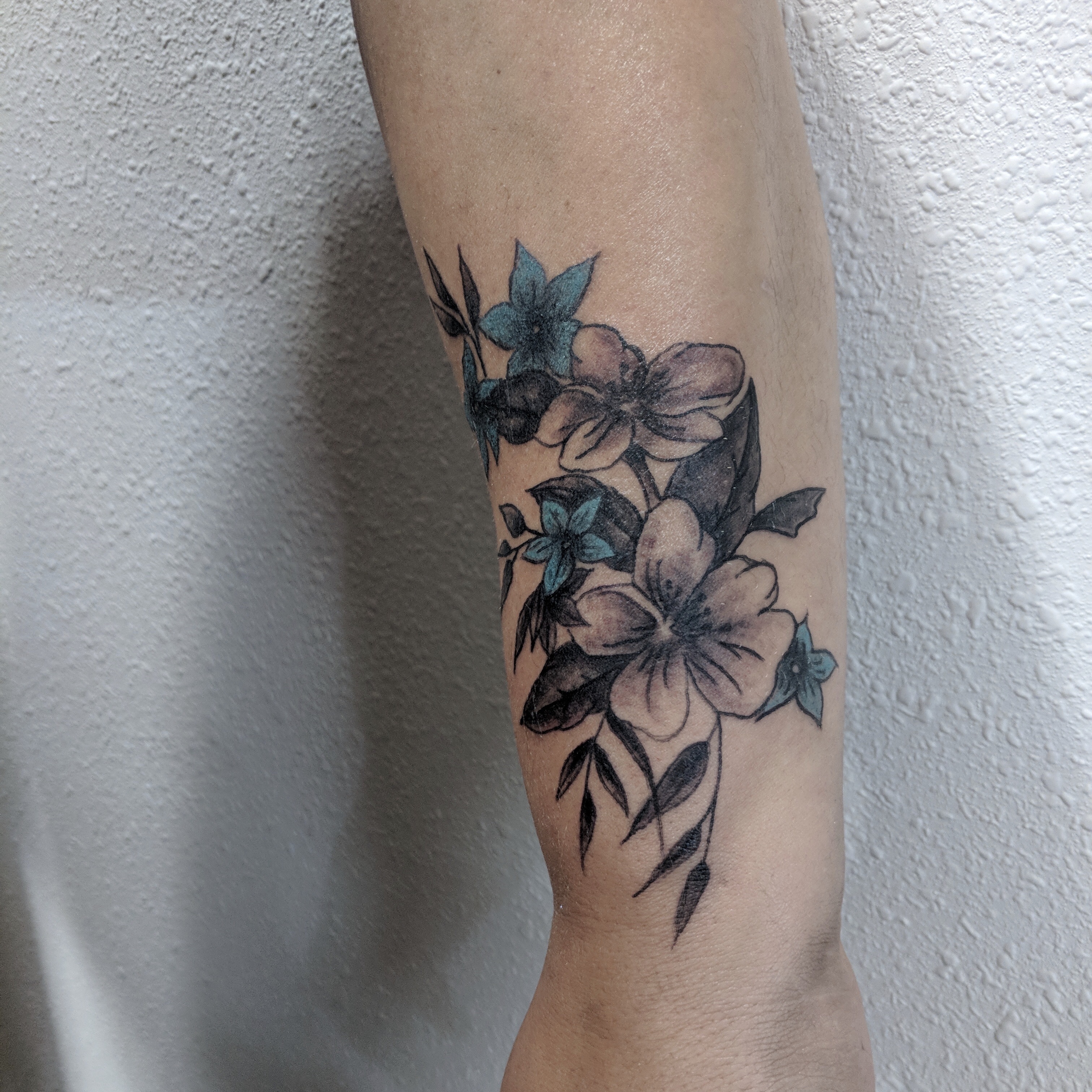 Image of a Floral tattoo on a wrist in black and grey with pops of blue